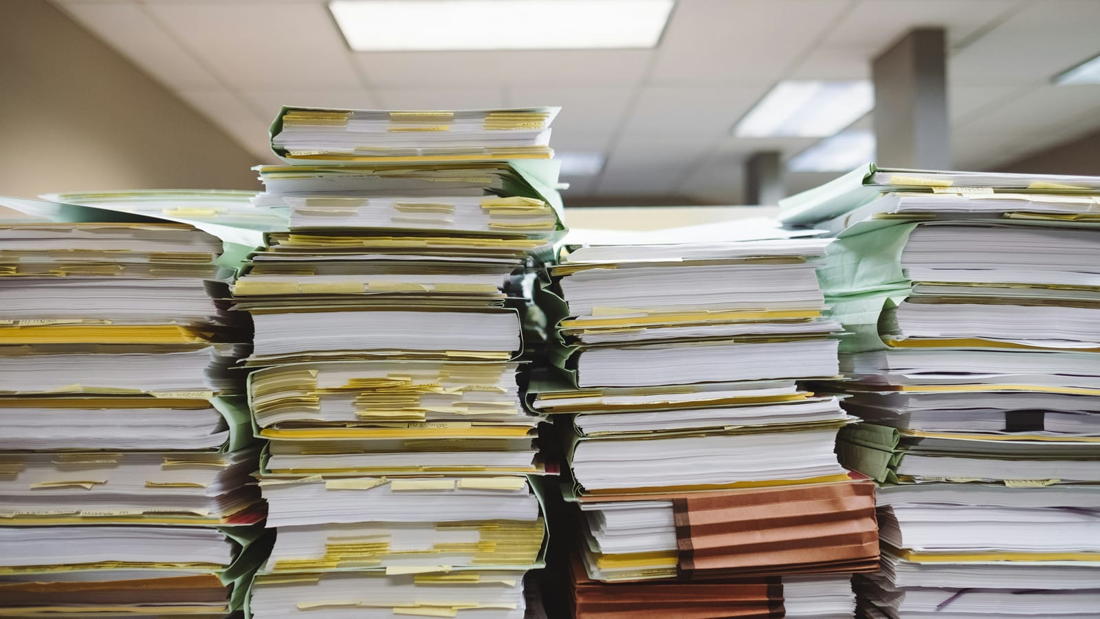 Tall stacks of tabbed paper files filling an office desk, the seven-year record-keeping obligation in physical form
