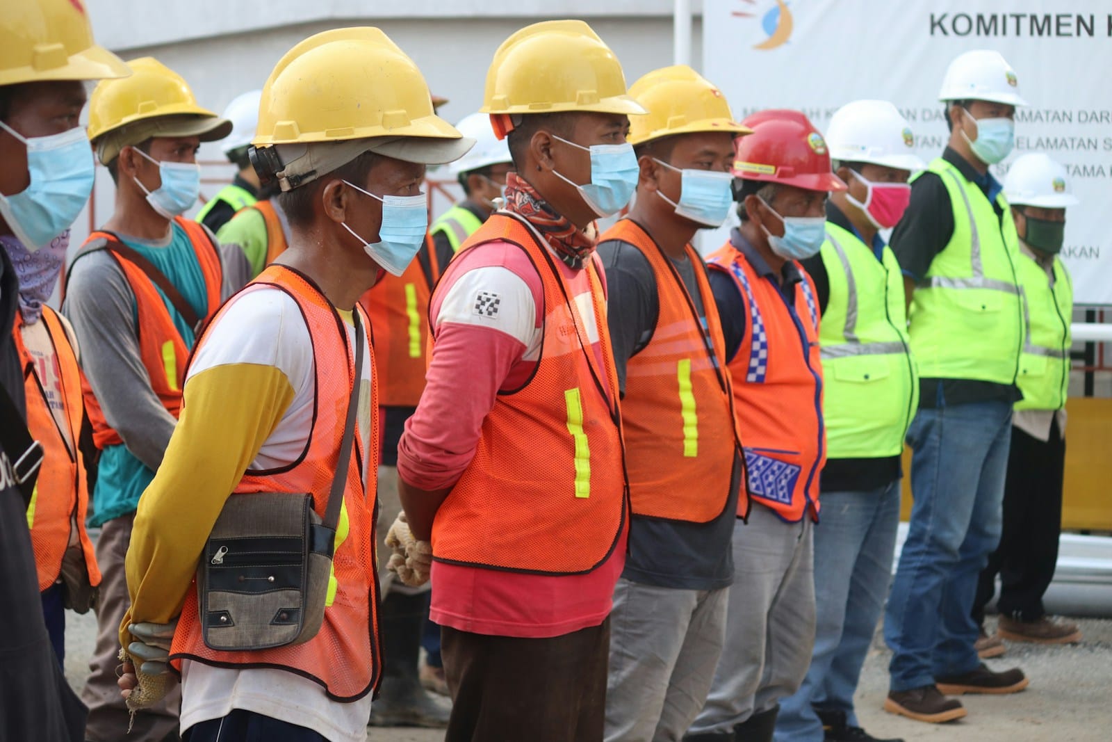 Group of labour hire workers in orange and yellow hi-vis vests gathered on a client site