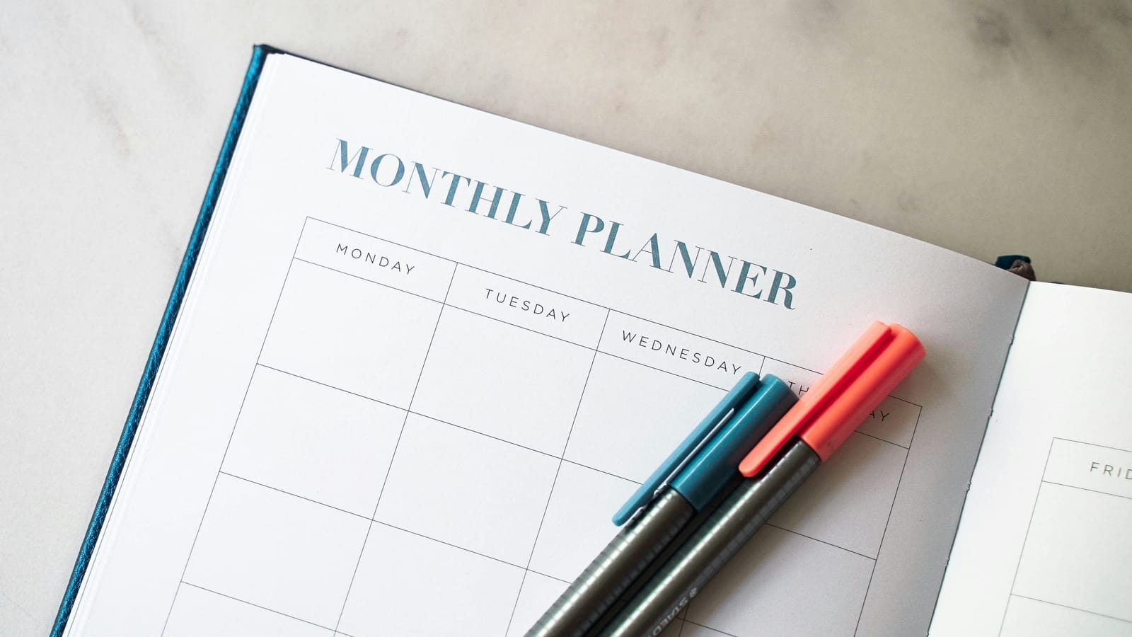 A paper monthly planner and pens, the manual roster that every change has to be re-checked against by hand