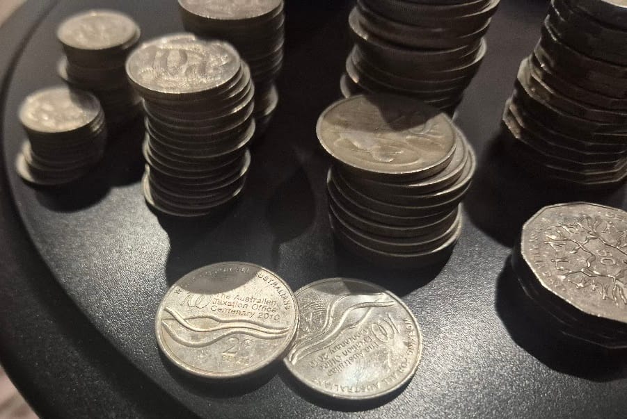 Stacks of Australian silver coins on a dark table, with two ATO Centenary 2010 twenty-cent pieces at the front, a coin the tax office minted for its own hundredth birthday