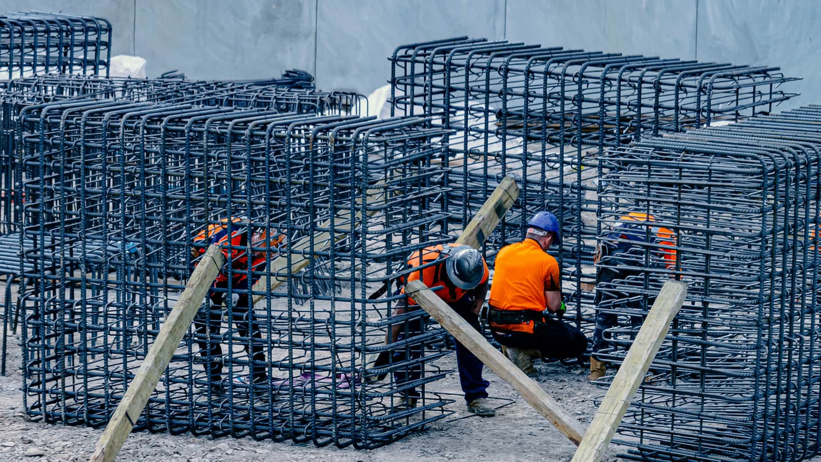 Steel fixers in hi-vis and hard hats tie reinforcement cages braced with timber props on a construction site