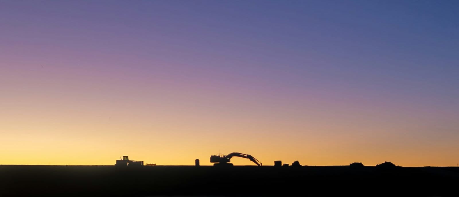 Earthmoving machinery silhouetted against the dusk sky at the end of a site day shift