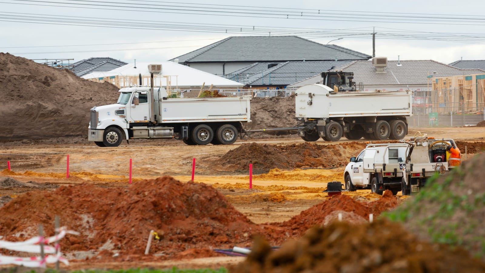 A truck-and-dog tipper and site utes moving earth on an Australian subdivision project