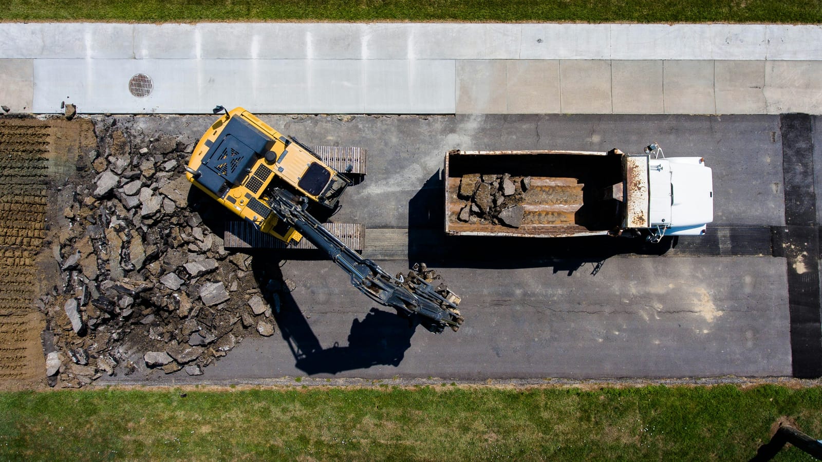 An excavator loading a tipper from above, one job with its machines working as planned