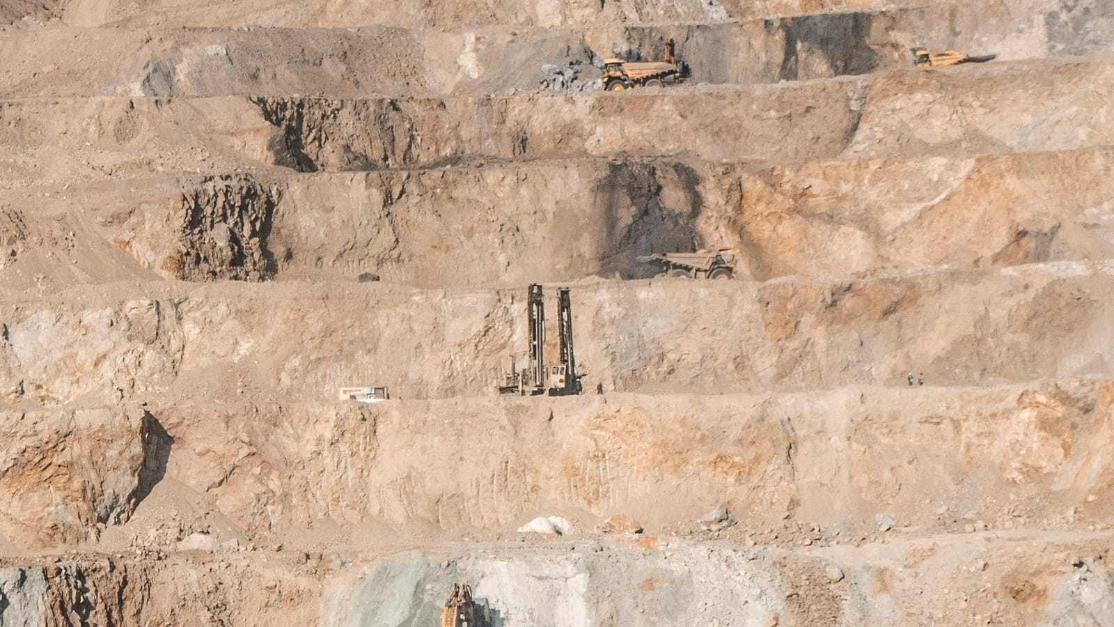 Benches of an open-cut mine with drill rigs and haul trucks working different levels